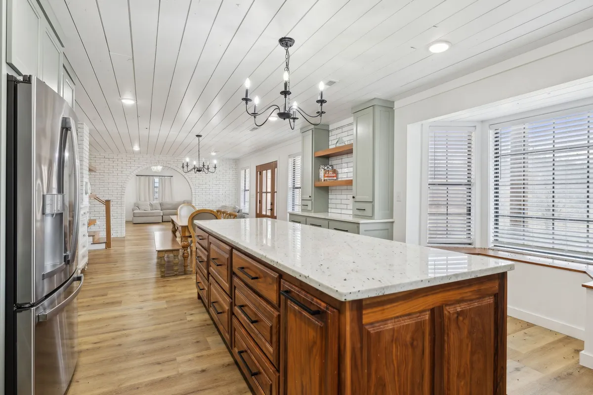 A spacious, inviting kitchen with a large island, elegant chandelier, and an adjoining dining area. The cabinetry and open layout make it ideal for meal preparation and group gatherings, while ample seating provides space for conversations and shared meals.