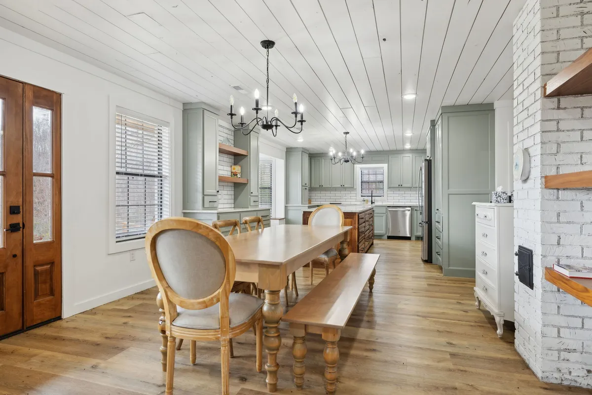 An inviting dining area with a large wooden table, a sparkling chandelier overhead, and a glimpse of the kitchen cabinetry. The space is well-lit and ideal for family meals, entertaining guests, and group celebrations.