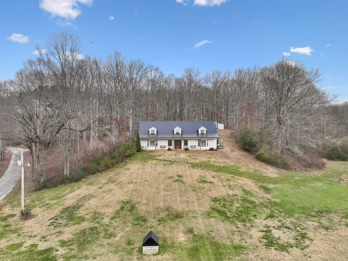 A peaceful exterior shot of the house framed by mature trees and an open field, capturing the spaciousness of the property. The setting sun casts a warm glow, highlighting the vast yard and providing a sense of tranquility and space for family activities.