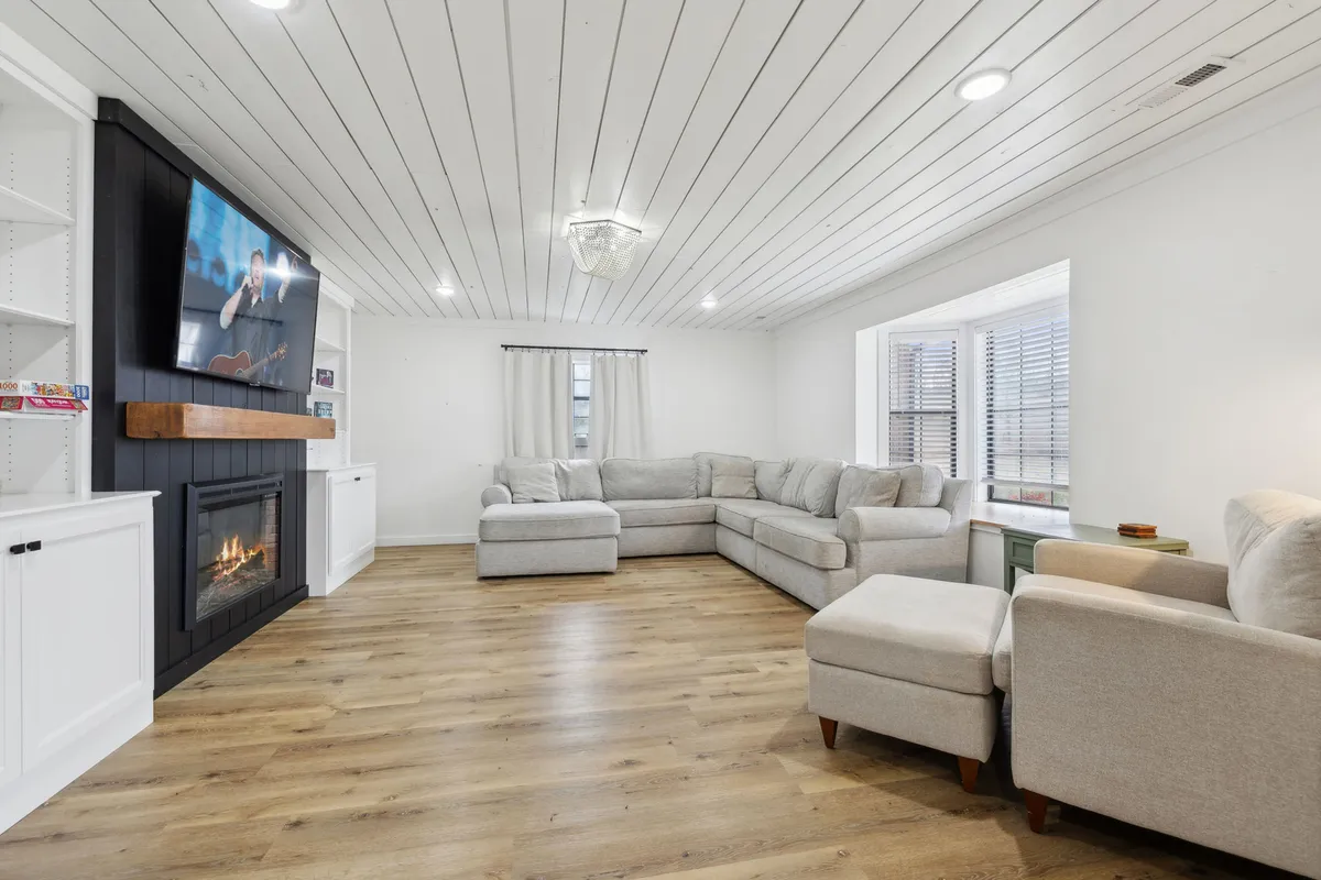 A spacious living room featuring a comfortable sectional sofa, a wall-mounted television, and a cozy fireplace. The room is designed for family gatherings, relaxation, and shared entertainment, with natural light streaming in and a welcoming ambiance.
