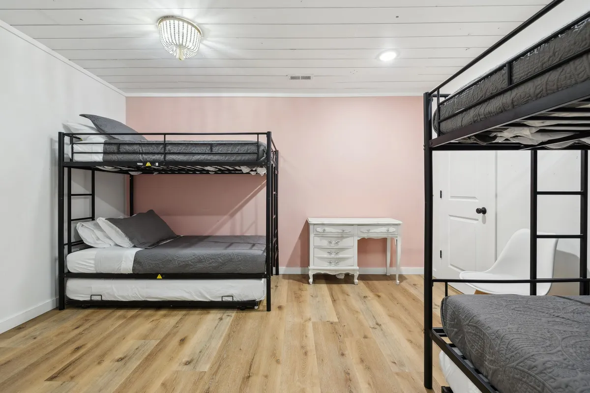 A vibrant bunk room with built-in bunk beds, a desk for studying or games, and a cheerful pink accent wall. The space is designed to be playful yet comfortable, perfect for multiple guests or children.