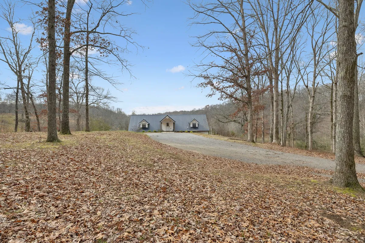 This exterior image captures the house nestled among tall trees, with a spacious driveway leading up to the property. The surrounding natural landscape hints at nearby trails and open spaces perfect for outdoor recreation and family activities.