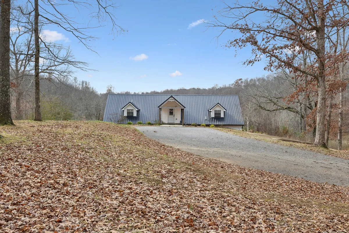 A wide shot of the house, driveway, and surrounding trees, evoking the tranquil seclusion of Fox Haven. The setting sun and open sky hint at opportunities for stargazing or enjoying peaceful evenings in nature.